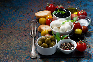 mozzarella, ingredients for the salad and bread on dark background