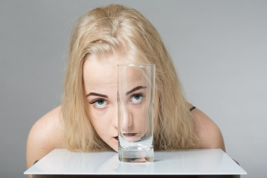 girl looks at camera through empty glass on gray background