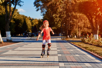 Girl riding on roller skates in skatepark summer outdoor. Child in a red suit for the rollers