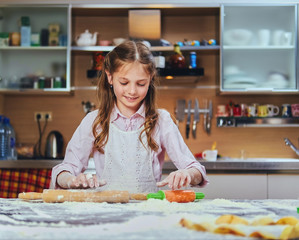 Cheerful little girl cooking dough at the kitchen.