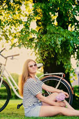 Obraz premium Portrait of brunette female sits on a lawn in a sunny park.