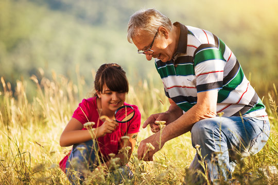 Happy grandfather and granddaughter explore together with magnifying glass nature.