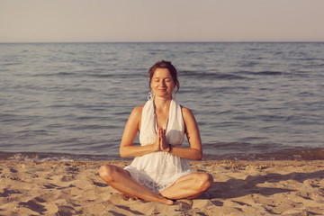 Fototapeta na wymiar Young woman meditating by the seashore in sunset