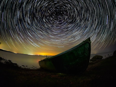 beautiful sky at night with startrails over the lake and silhouette of fishing boat
