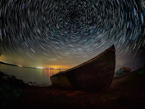 beautiful sky at night with startrails over the lake and silhouette of fishing boat
