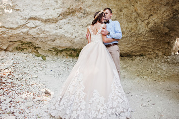 Beautiful bride with handsome groom posing next to the cave in forest on their wedding.