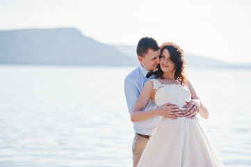 Amazing young couple holding hands on the lake shore on their sunny wedding day.