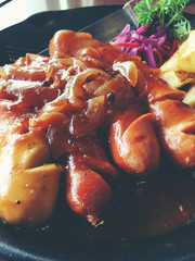 Fried sausages with garlic, herbs and french fries in a pan on the table black Board. still life food. vintage tone.