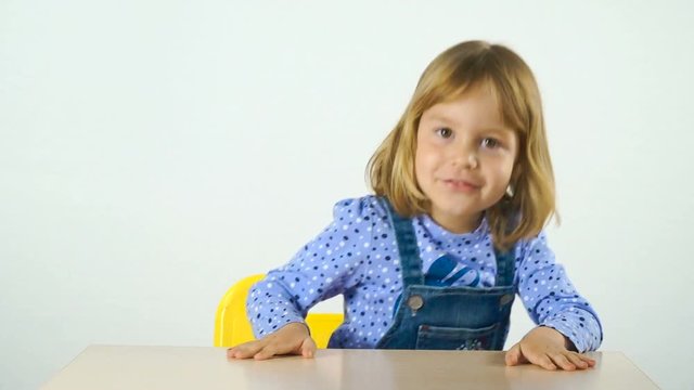 A cheerful Russian girl 4-5 years old posing on the camera, sitting at the table. Shooting on white background.