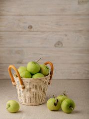 Green apples in a wicker basket on a wooden light background.