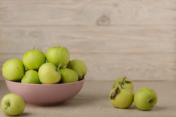 Green apples in a lilac plate on a wooden light background.