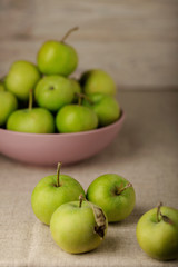 Green apples in a lilac plate on a wooden light background.