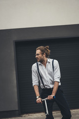 Handsome stylish young man in formal wear and eyeglasses riding scooter and looking away