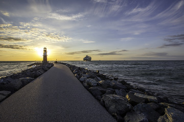 Schiff verlässt den Hafen von Warnemünde hinter einem Leuchtturm im Sonnenuntergang