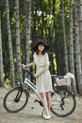 Fototapeta premium Outdoor portrait of attractive young brunette in a hat on a bicycle.