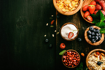 Healthy classic breakfast with oatmeal, cornflakes and various fresh berries on a black wooden surface. Toned.