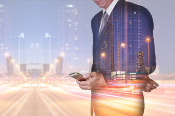 Double exposure of businessman stand up and research by smartphone, light trails on the street and urban at dusk, night as technology, communication and business concept.