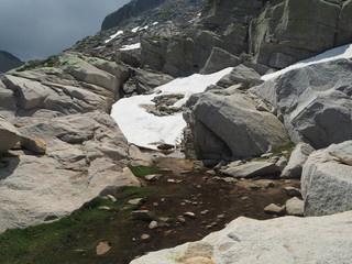 mountain snow tongue with boulders water stream and green grass