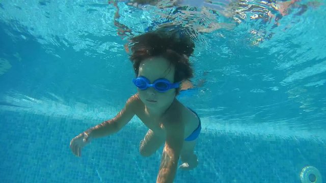 A little boy in swimming goggles playing under water in the swimming pool
