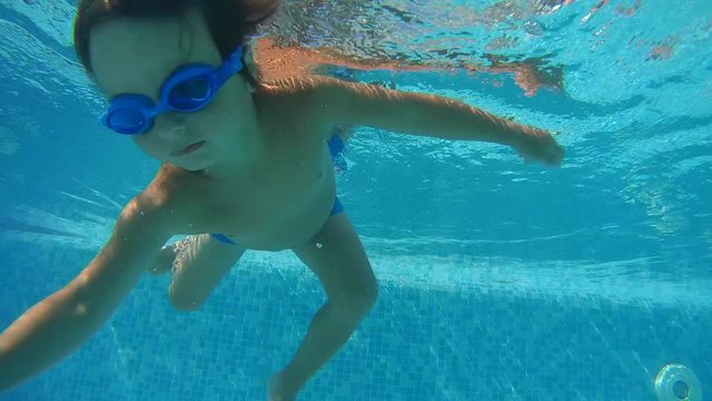 A little boy in swimming goggles playing under water in the swimming pool
