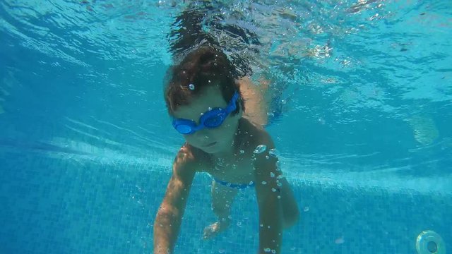 A little boy in swimming goggles playing under water in the swimming pool
