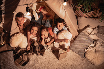 multiethnic group of children resting in handmade tent together at home