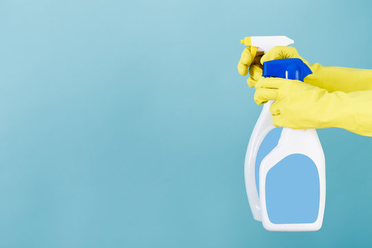 Hand in yellow glove holds  spray bottle of liquid detergent on blue background. cleaning