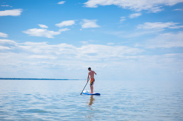 A young guy is floating on a sup board against the blue sky