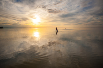 A loving couple is swimming on a sup board in the sea or the ocean against a sunset background