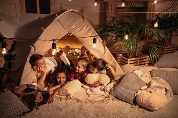multiethnic group of children resting in handmade tent together at home