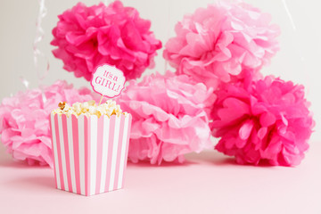 It's a girl sign in a popcorn bag at the baby shower party.  Paper flowers background.  Baby shower celebration concept