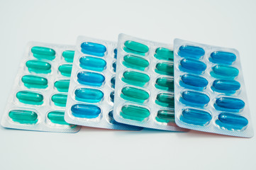 Blue and green soft gelatin capsules in blister pack on white background