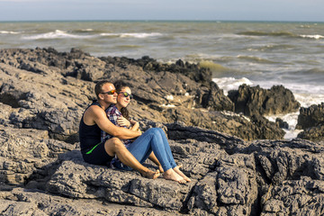 Portrait of young and happy couple sitting on the rocks next to the sea. France.