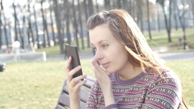 Girl makes selfie outside, sitting on bench in park