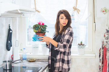 Young woman decorating her kitchen. Portrait of girl holding flower pot indoors.