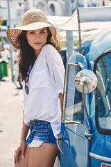 Traveling young woman stands by an old Italian blue car