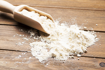 Wooden spoon with flour on brown wooden table.