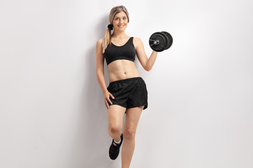 Young woman with a dumbbell leaning against a white wall
