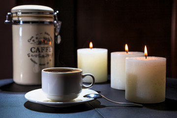 Cup of coffee costs on a table on a background of burning candles
