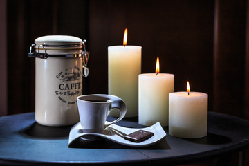 Cup of coffee costs on a table on a background of burning candles