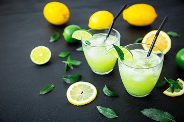 Fresh citrus lemonade with limes and lemons in glasses on dark background