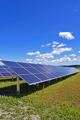 Solar panels on field. Clear sky with a few small clouds on background. Vertical image.