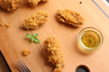 Wings of chicken in breading on a wooden background, butter and basil
