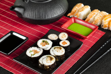 Sushi set and black teapot on red mat and black table