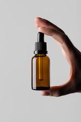 Dropper Bottle Mock-Up - Male hands holding a dropper bottle on a gray background