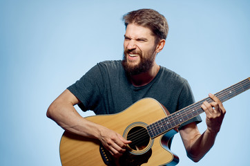 Young guy with a beard on a blue background plays the guitar