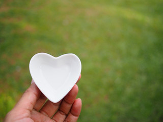 Female hand holding a white ceramic heart on garden background