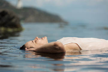 A young woman is swimming in the sea. She lies on her back.