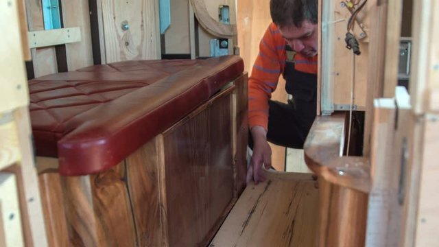 A woodworker is making sure the wooden floor in the vintage car that he is making is even and that there are no bumps. 