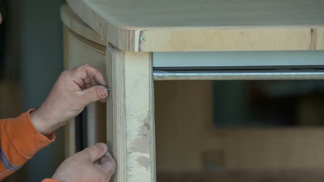 A man is building a vintage car and he is putting in a couple of screws in two wooden palets. 